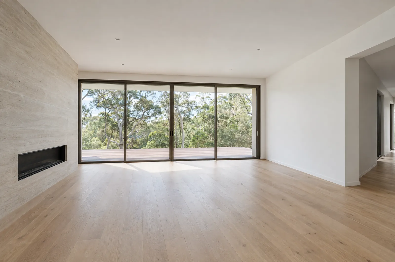 AI-generated example of an empty living room: pale oak floorboards, a limestone fireplace wall and glass sliding doors to a deck and eucalypts.